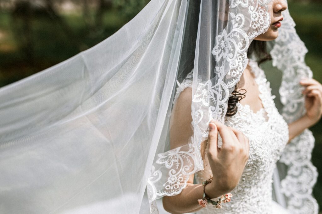 Bride in lace wedding dress holding a sheer veil.
