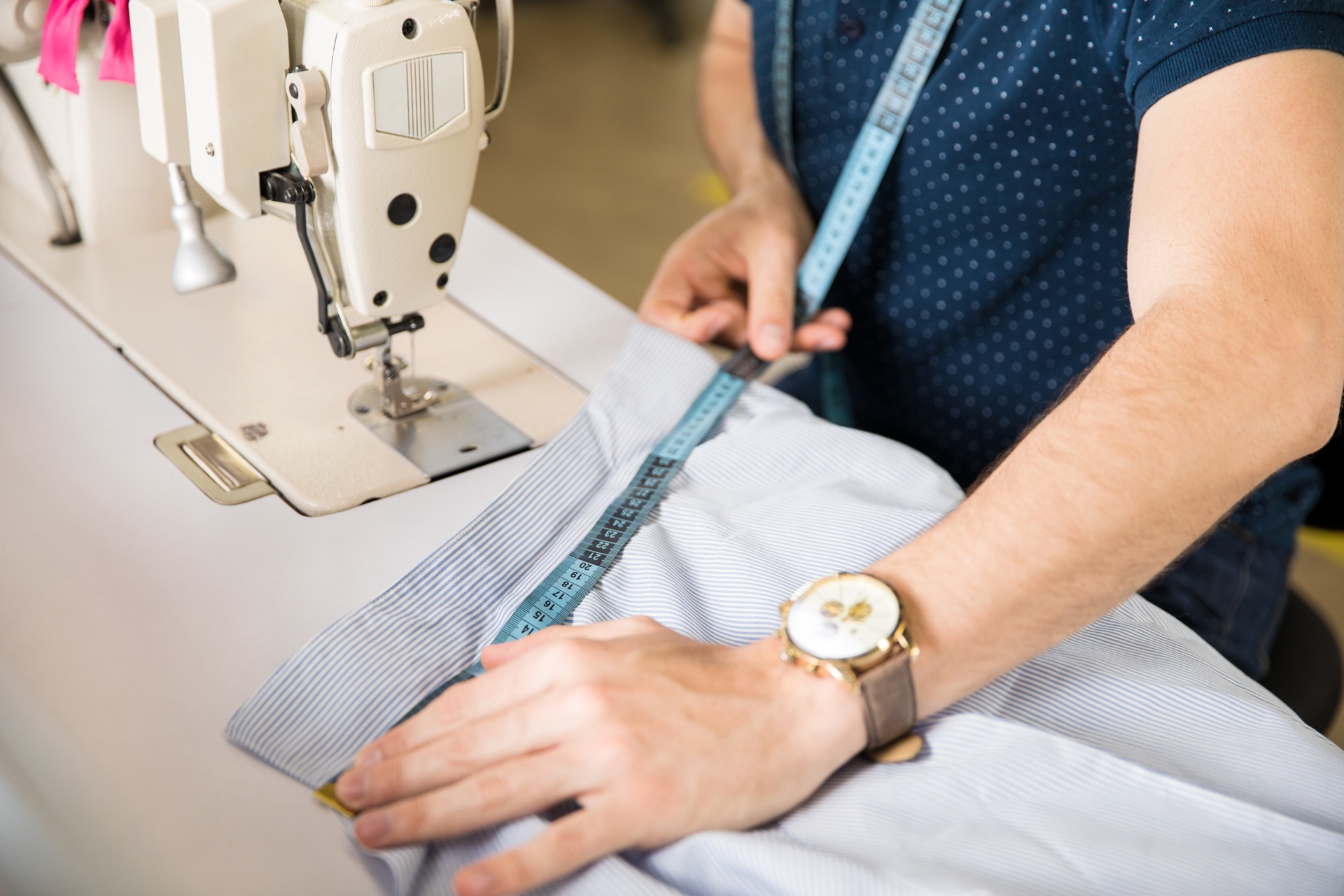 A person measures fabric with a measuring tape next to a sewing machine, preparing for garment alterations.