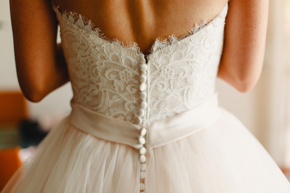Close-up of the back of a person wearing a white lace wedding dress with button details and a satin waistband.