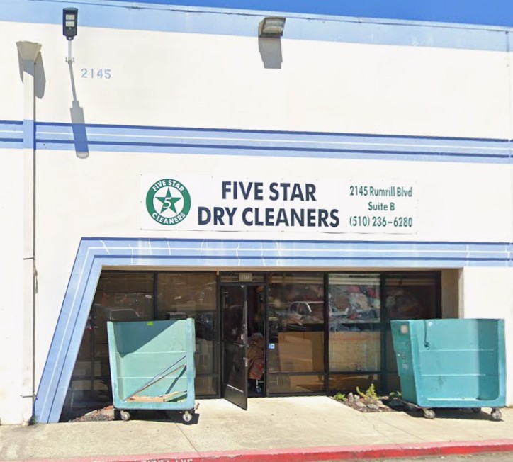 Front view of Five Star Dry Cleaners with open double doors, two large green bins outside, and the business sign displaying address and phone number.