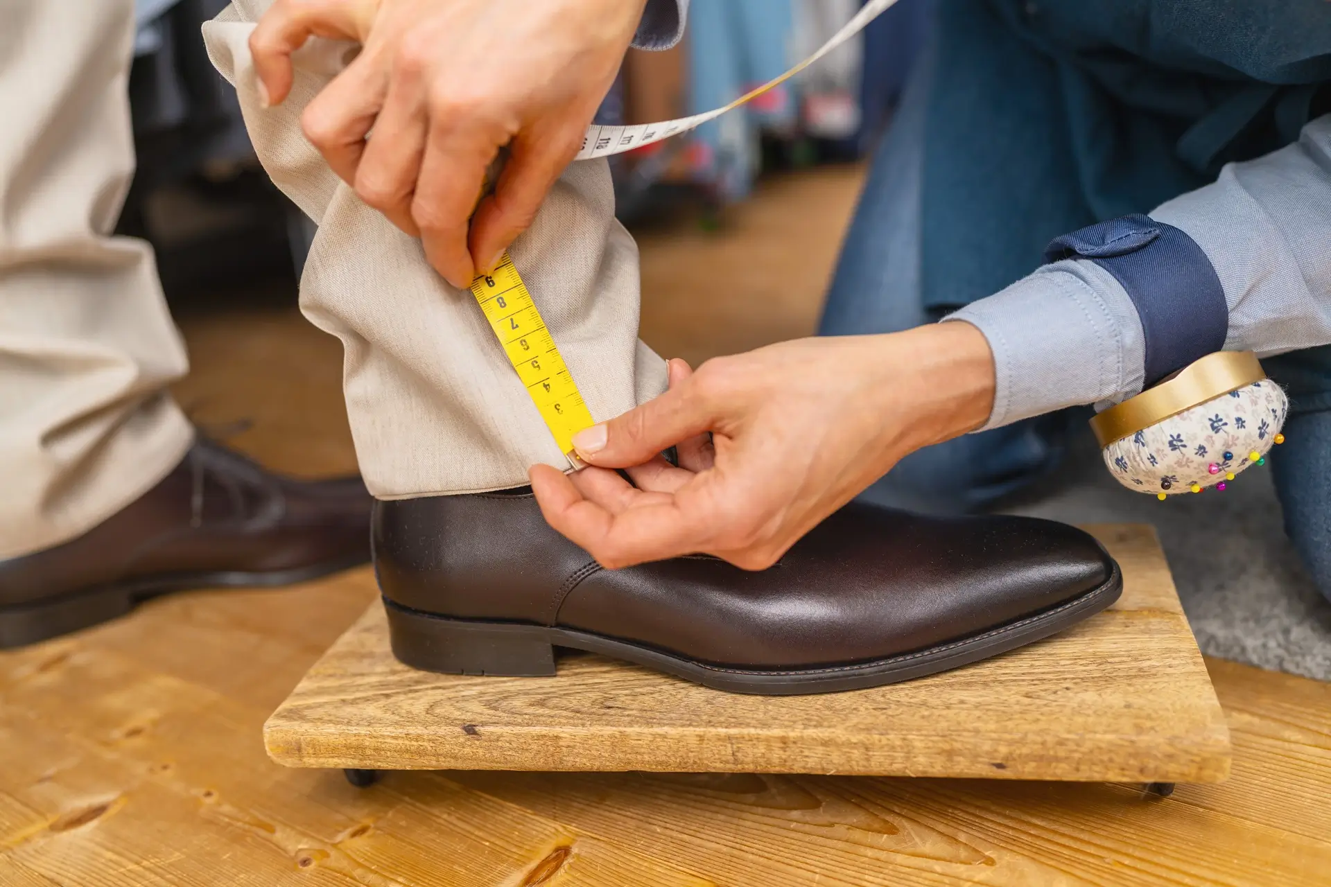 Tailor measuring the inseam of a person’s beige pants while they wear dark brown dress shoes, using a yellow tape measure. Tailor measuring the inseam of a person’s beige pants while they wear dark brown dress shoes, using a yellow tape measure.